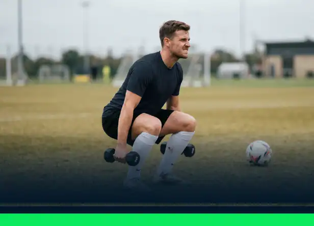 Joueur de football en position basse de squat tenant deux haltères
