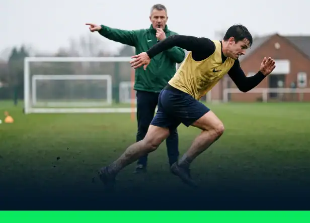 Joueur de foot en plein démarrage explosif sur un terrain d'entraînement, corps penché en avant, bras en mouvement